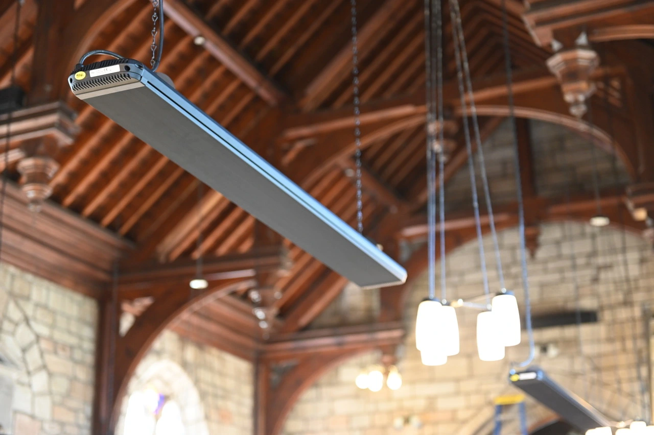 Aquecedor SRP eWave suspenso sob um teto de madeira, com o perfil de alumínio anodizado negro visível